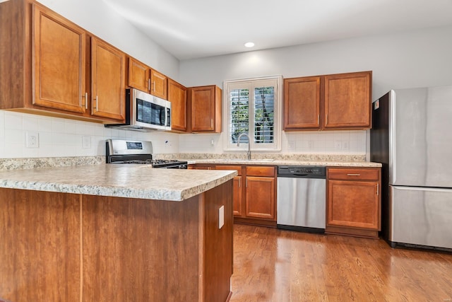 kitchen with sink, kitchen peninsula, tasteful backsplash, appliances with stainless steel finishes, and light wood-type flooring