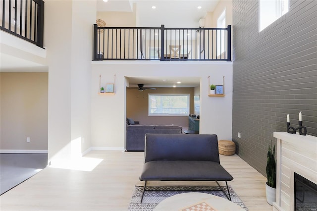 living room featuring ceiling fan, brick wall, a high ceiling, and light wood-type flooring