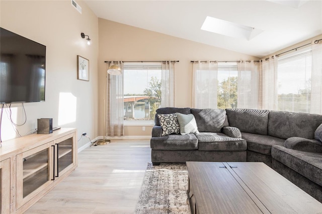 living room featuring vaulted ceiling with skylight and light hardwood / wood-style floors