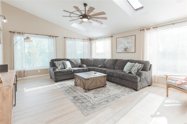 living room with ceiling fan, vaulted ceiling with skylight, and light wood-type flooring