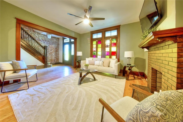 living room with light hardwood / wood-style flooring, a brick fireplace, and ceiling fan