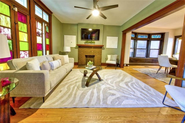 living room with light hardwood / wood-style flooring, a brick fireplace, and ceiling fan