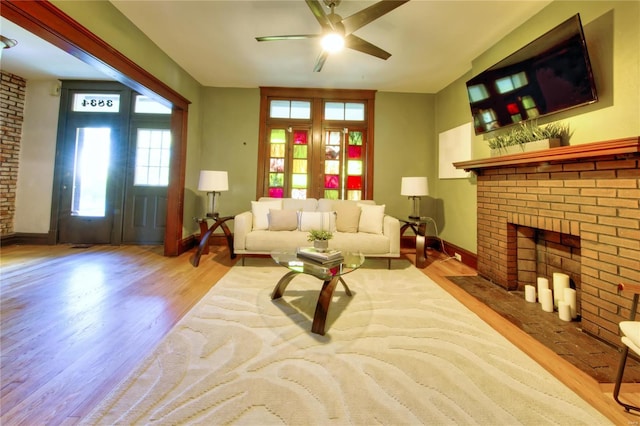 living room with light hardwood / wood-style floors, a brick fireplace, and ceiling fan