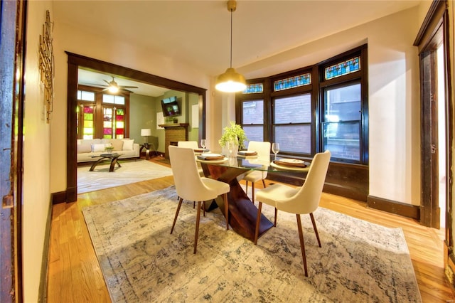 dining space featuring ceiling fan, a brick fireplace, light wood-type flooring, and plenty of natural light