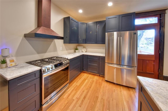 kitchen with light hardwood / wood-style floors, wall chimney exhaust hood, light stone countertops, and stainless steel appliances