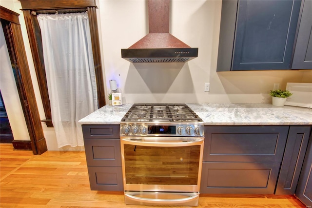 kitchen with high end stainless steel range oven, light stone countertops, wall chimney exhaust hood, and light wood-type flooring