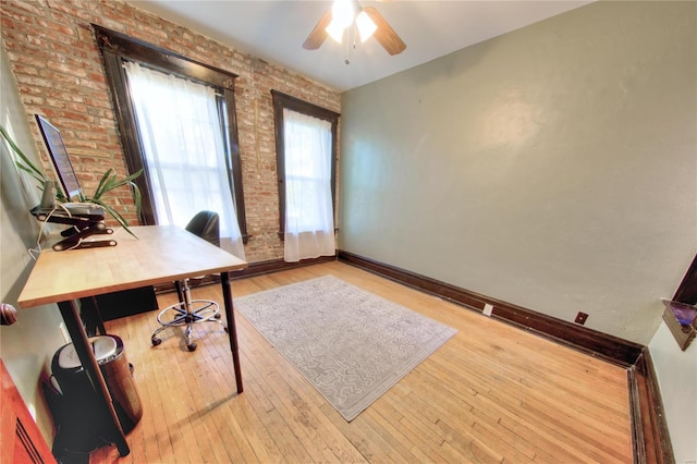 office area with brick wall, light hardwood / wood-style floors, and ceiling fan