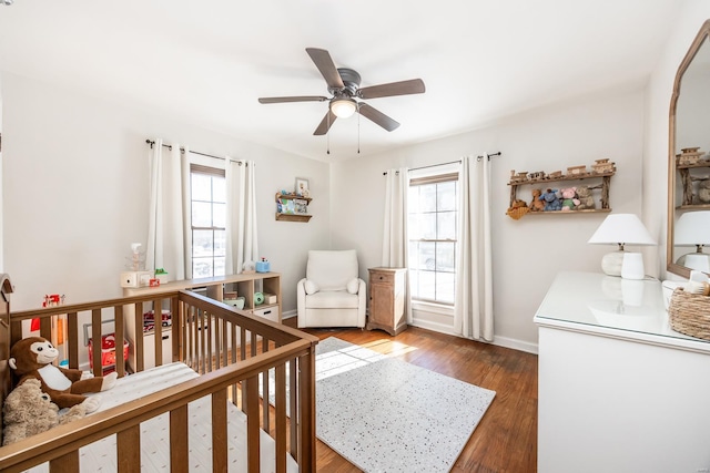 bedroom featuring dark hardwood / wood-style floors, ceiling fan, and a nursery area