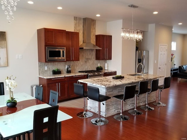 kitchen with appliances with stainless steel finishes, an island with sink, wall chimney exhaust hood, light hardwood / wood-style flooring, and sink