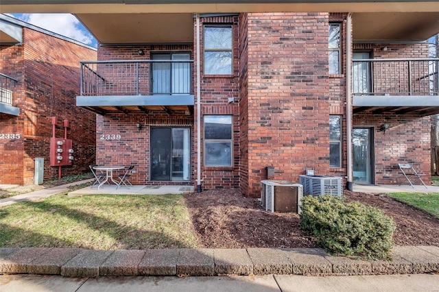 rear view of property with a balcony, central AC unit, and a lawn