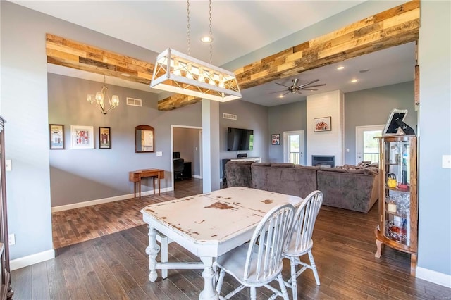 dining space with ceiling fan with notable chandelier, beamed ceiling, a fireplace, and dark wood-type flooring