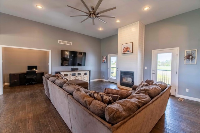 living room with a towering ceiling, dark hardwood / wood-style floors, ceiling fan, and a large fireplace