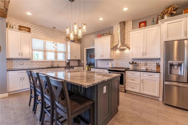 kitchen featuring sink, a kitchen island, decorative light fixtures, wall chimney exhaust hood, and appliances with stainless steel finishes