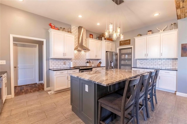 kitchen with appliances with stainless steel finishes, wall chimney exhaust hood, a center island, and white cabinetry