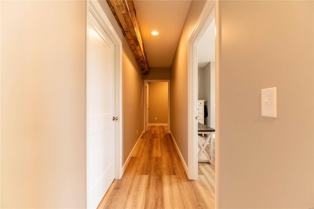 corridor with light hardwood / wood-style flooring and beam ceiling