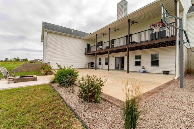 back of property featuring a balcony, a patio, an outdoor fire pit, and a lawn