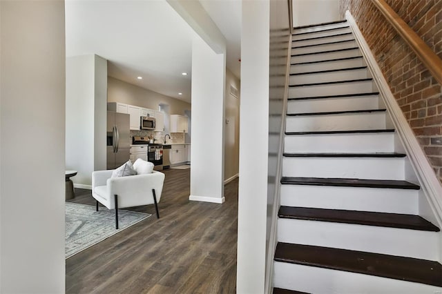 stairway with wood-type flooring, brick wall, and sink