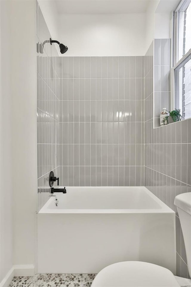 bathroom with tile patterned flooring, tiled shower / bath, and toilet