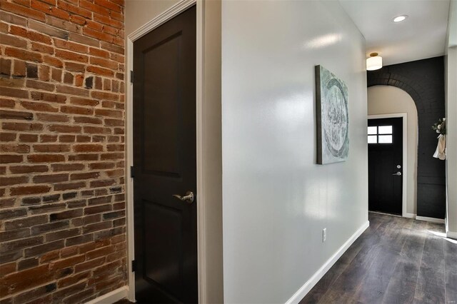 hallway with brick wall and dark wood-type flooring