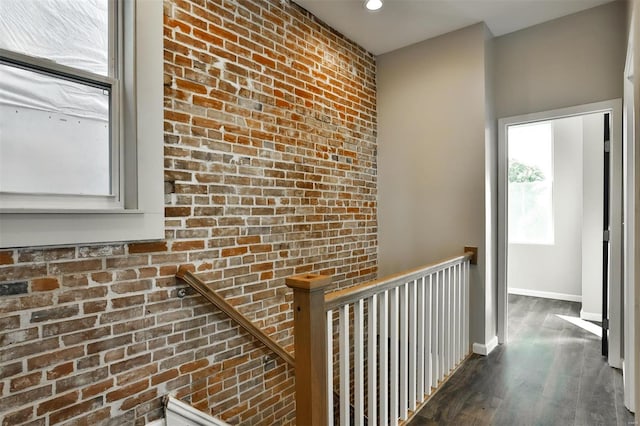 hallway with dark wood-type flooring and brick wall