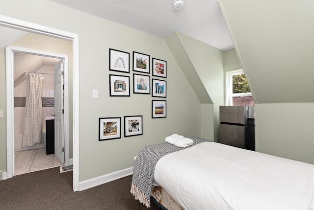 bedroom with lofted ceiling, stainless steel fridge, connected bathroom, and carpet floors