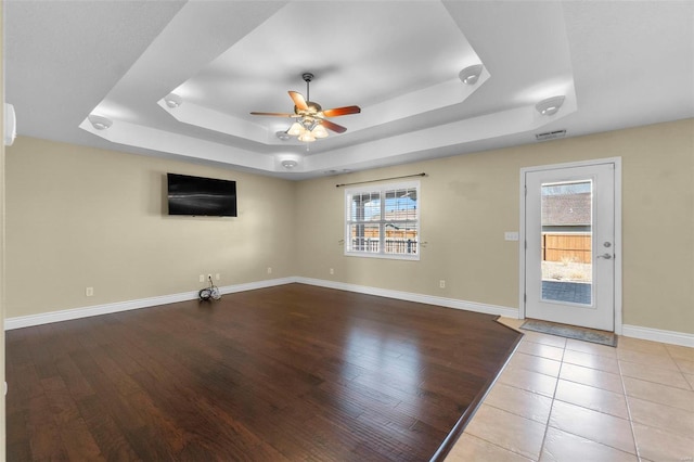 unfurnished living room featuring a wealth of natural light, light hardwood / wood-style floors, and a raised ceiling