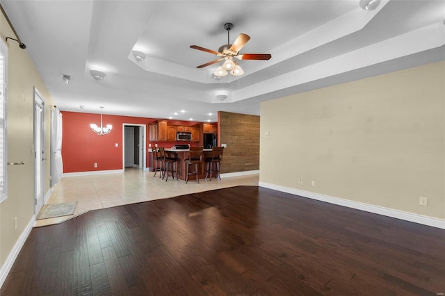 unfurnished living room with a raised ceiling, ceiling fan with notable chandelier, and light hardwood / wood-style floors