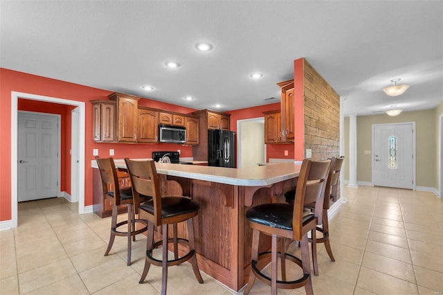 kitchen featuring range with electric cooktop, a kitchen breakfast bar, black fridge with ice dispenser, and light tile patterned flooring