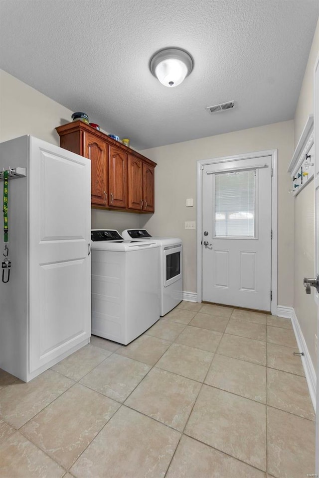 laundry room with cabinets, washing machine and dryer, light tile patterned flooring, and a textured ceiling