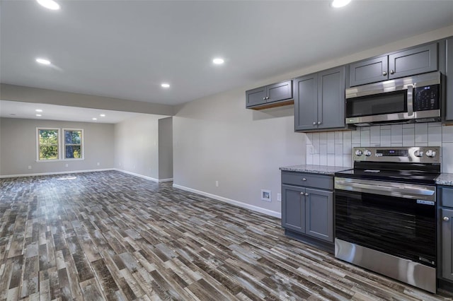 kitchen featuring backsplash, appliances with stainless steel finishes, dark hardwood / wood-style flooring, gray cabinets, and light stone counters