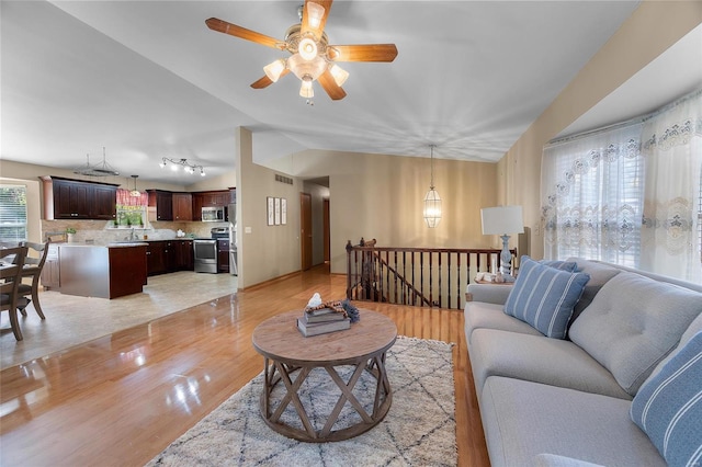 living room with sink, vaulted ceiling, light hardwood / wood-style flooring, and ceiling fan