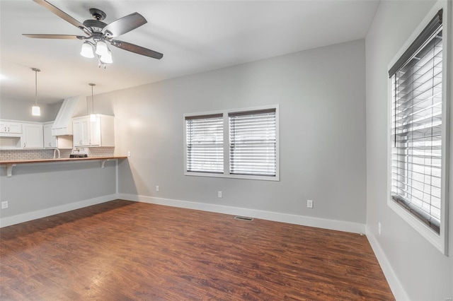 unfurnished living room featuring dark wood-style flooring, a ceiling fan, baseboards, and visible vents