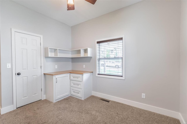 unfurnished office featuring light colored carpet, built in study area, a ceiling fan, baseboards, and visible vents