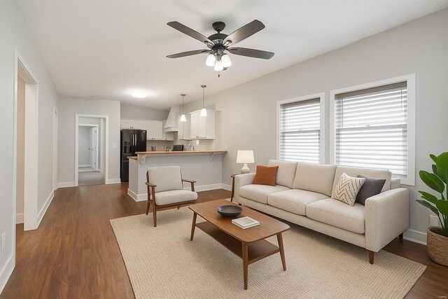 living room featuring baseboards, ceiling fan, and dark wood-style flooring
