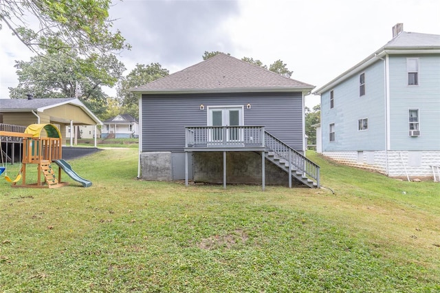 back of property with a deck, a playground, a yard, a shingled roof, and stairs