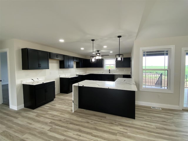 kitchen with light wood-type flooring, light stone counters, a kitchen island, decorative light fixtures, and ceiling fan