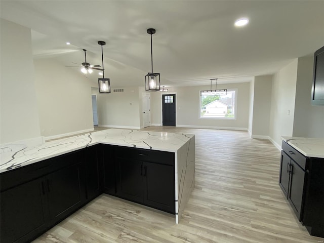 kitchen featuring light stone countertops, ceiling fan with notable chandelier, pendant lighting, and light hardwood / wood-style floors