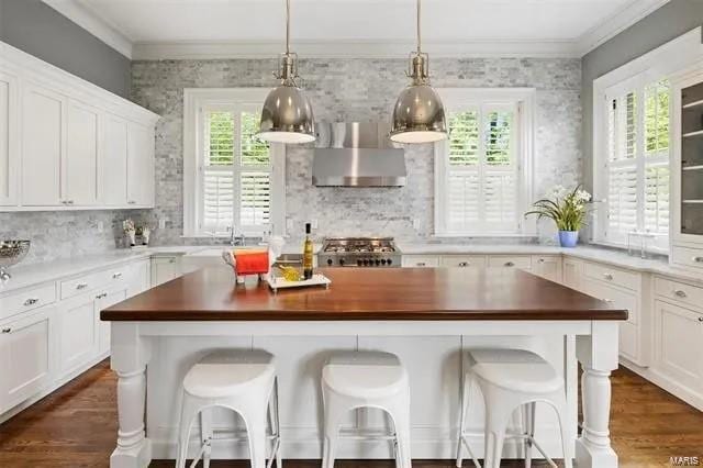 kitchen featuring white cabinetry, a breakfast bar area, wall chimney range hood, and plenty of natural light