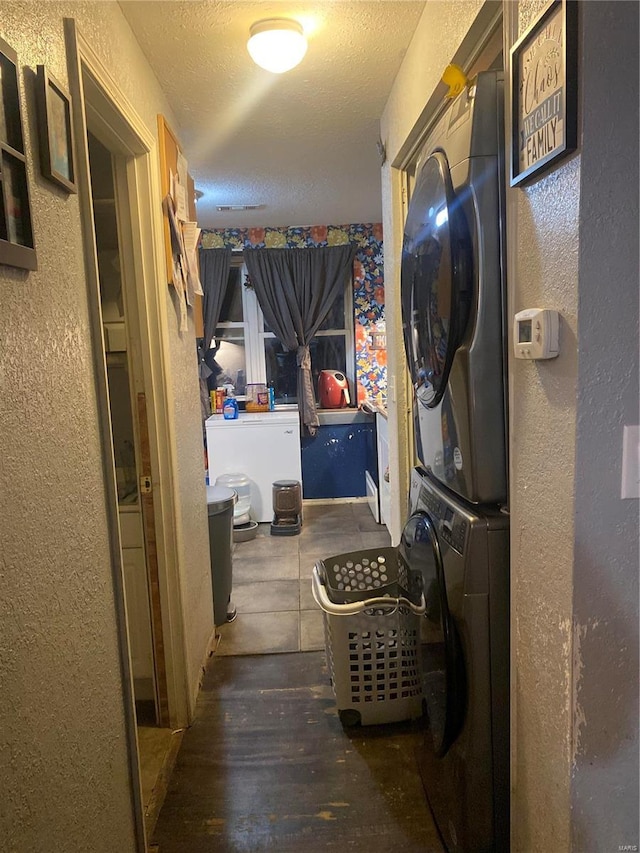 laundry area with a textured ceiling, stacked washer and clothes dryer, and dark wood-type flooring