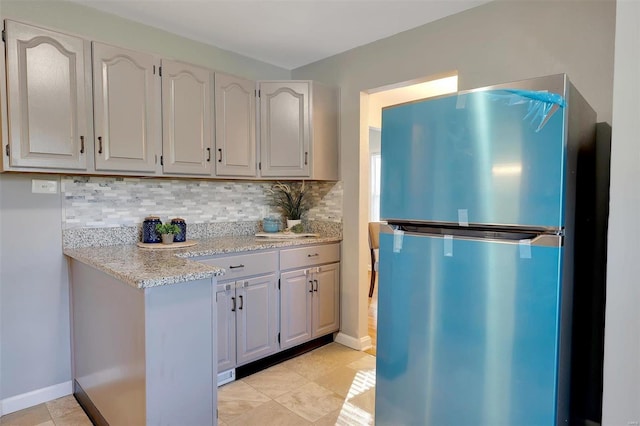 kitchen featuring decorative backsplash, light stone countertops, and stainless steel fridge