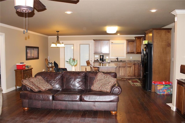 living room with ceiling fan with notable chandelier, ornamental molding, dark wood-type flooring, and sink