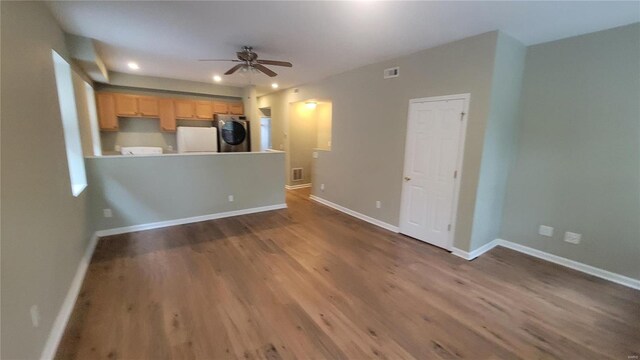 unfurnished living room with ceiling fan, stacked washer and dryer, and hardwood / wood-style flooring