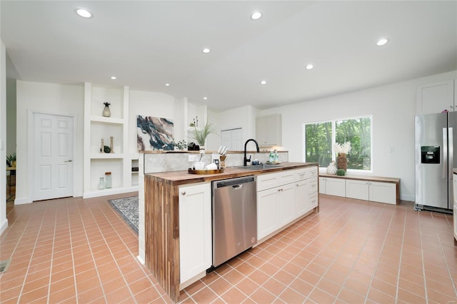 kitchen featuring light tile patterned flooring, sink, white cabinets, appliances with stainless steel finishes, and butcher block countertops