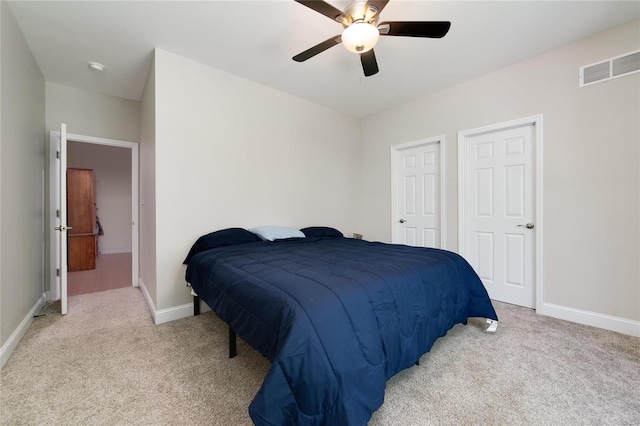 bedroom featuring ceiling fan, light colored carpet, and two closets