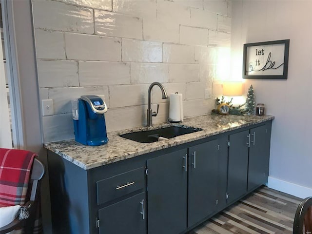 bar with dark wood-type flooring, light stone countertops, blue cabinets, and sink