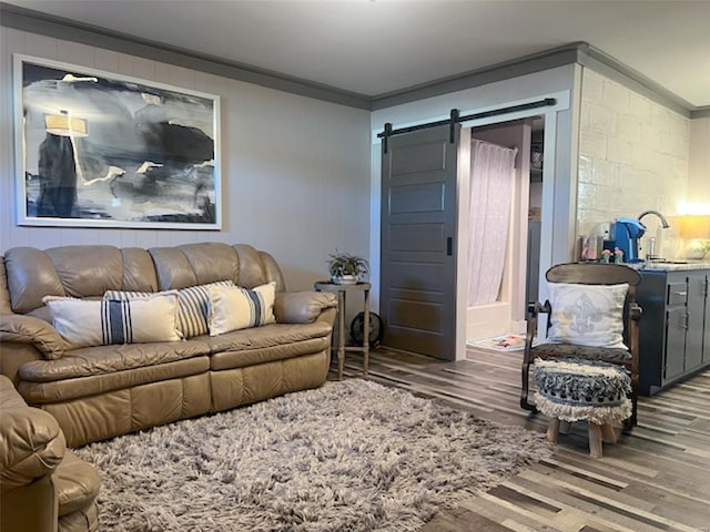 living room featuring hardwood / wood-style flooring, crown molding, a barn door, and sink