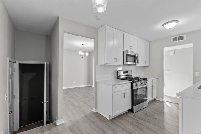 kitchen with light hardwood / wood-style floors, white cabinets, decorative backsplash, an inviting chandelier, and appliances with stainless steel finishes