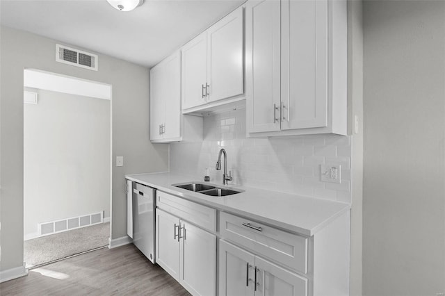 kitchen with light hardwood / wood-style floors, white cabinetry, backsplash, dishwasher, and sink