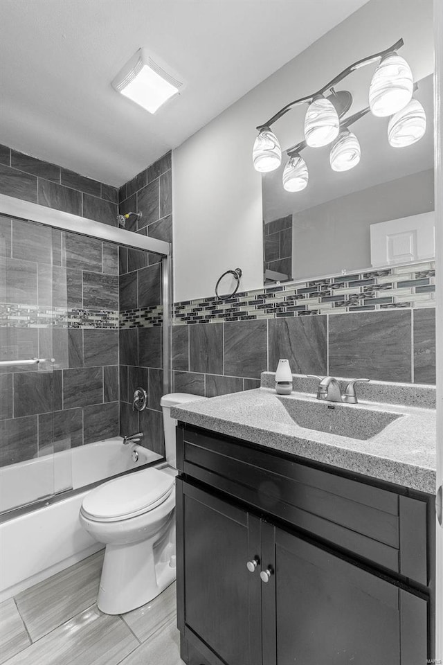 full bathroom with tile walls, bath / shower combo with glass door, vanity, and toilet