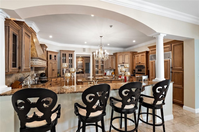 kitchen featuring premium range hood, pendant lighting, ornate columns, dark stone countertops, and a kitchen bar